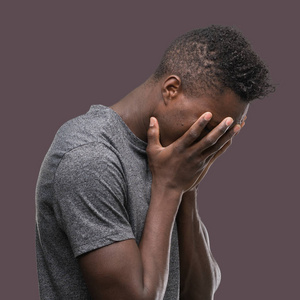年轻的非洲裔美国人穿着灰色 t恤, 脸上带着悲伤的表情, 哭着捂着手。抑郁症概念