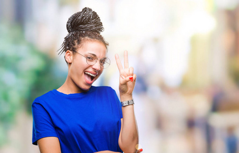 年轻的编织头发非洲裔美国女孩戴着眼镜在孤立的背景微笑与快乐的脸眨眼在相机做胜利标志。第二个