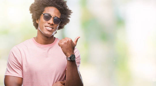 美国黑人戴着太阳镜在孤立的背景下微笑着快乐的脸, 用拇指指向侧面