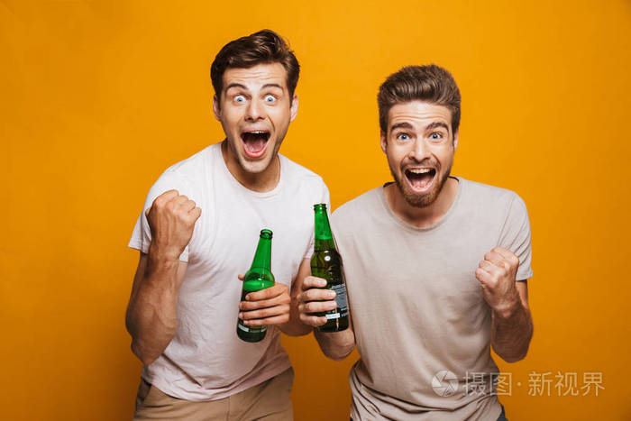 两个快乐的年轻人的肖像最好的朋友敬酒与啤酒瓶庆祝孤立的黄色背景