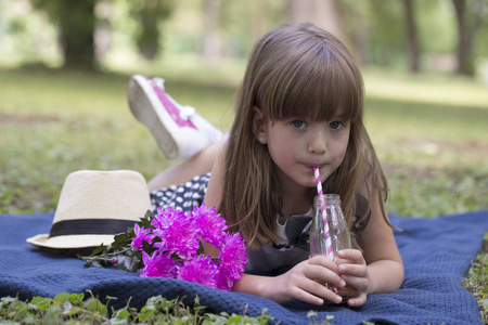 小可爱的女孩躺在公园的草地上喝果汁