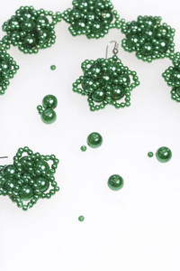 耳环和手镯手工制作。在家里做针线活。珠首饰。绿色。在白色背景上。珠子散落在附近