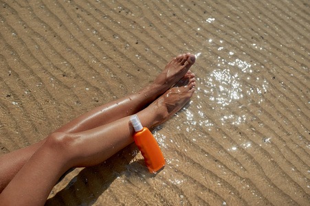 美丽的, 打扮女人的腿与奶油, 以保护晒太阳在夏天在背景海。关心清洁和柔软的皮肤。文本的空位置