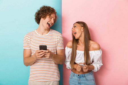 一对笑的年轻夫妇站在两个彩色背景, 使用手机, 看着对方的肖像