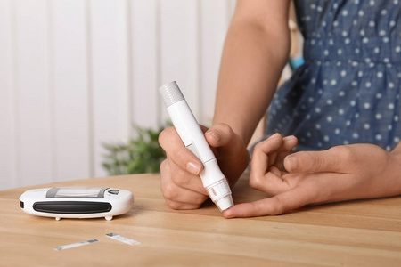 妇女使用柳叶刀笔在桌子上。糖尿病测试