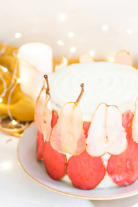节日的白色蛋糕, 用红白的梨片装饰在柔和的灯光和蜡烛之间的白色背景上