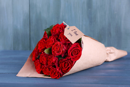 带有标记的红玫瑰花束裹在纸上木制背景