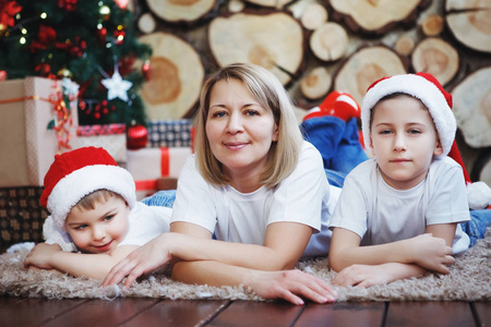 母亲与两个儿子在圣诞节帽子躺在树削减的背景下, 在新的一年树