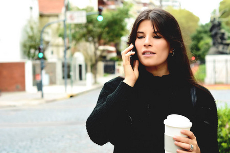 年轻的拉丁妇女的肖像与她的手机和咖啡杯。户外