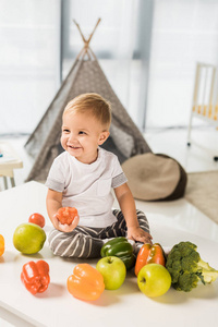 可爱的微笑的幼儿坐在桌子上, 周围是水果和蔬菜