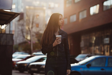 妇女享受步行与咖啡杯在城市街道