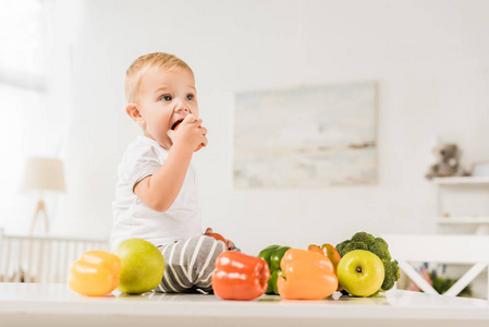 可爱的幼儿吃饭和坐在桌子上周围的水果和蔬菜