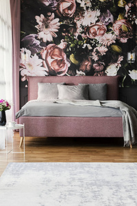 花壁纸在女性粉红色卧室内部与灰色枕头在床上。真实照片