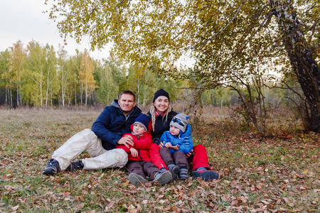 幸福的家庭带着两个孩子坐在秋天的森林里, 微笑着的人们