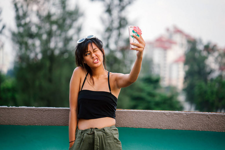 年轻的亚洲妇女在休闲服装制作自拍智能手机