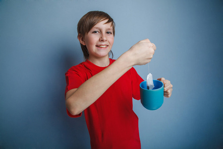 十几岁的男孩在一件红色的衬衫，捧着一杯茶，十二年