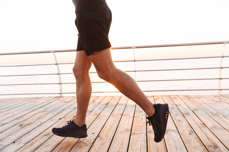 裁剪照片的肌肉运动男子20s 在短裤和 t恤上运行沿码头或散步道在海边的早晨