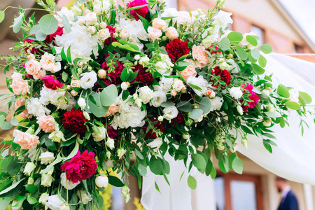 拱门上的花束特写镜头, 用白玫瑰和红牡丹作为参观仪式, 在这两个仪式之间, 有绿叶的树枝