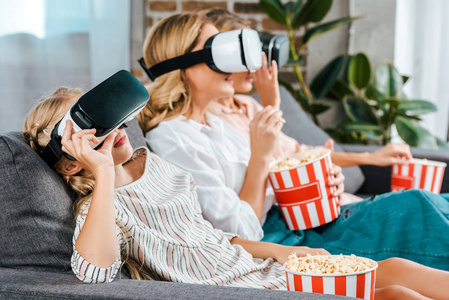 小孩子与母亲和祖母坐在沙发上一起看电影与虚拟现实耳机在家中