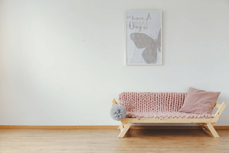 明亮的房间内部的真实照片的孩子, 木沙发, 柔和的粉红色毯子, 靠垫和灰色绒球和海报挂在墙上。您的产品的空位置