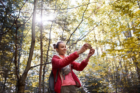 快乐微笑的女人在一个红色的夹克走在秋天的森林