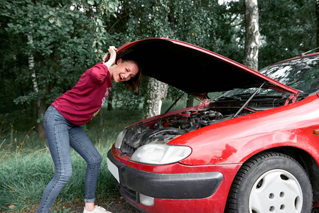 一个年轻的女孩站在一辆破车上, 看着发动机, 不懂怎么修理。