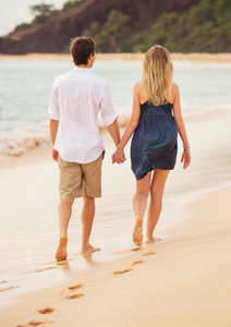 浪漫的幸福的夫妇，在日落时分在海滩上散步。微笑着握着