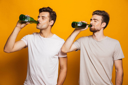 两个英俊的男人朋友的形象站在黄色墙背景喝啤酒