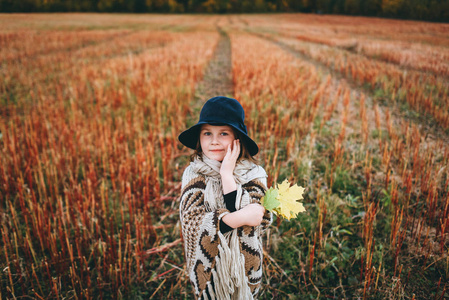 微笑的女孩的肖像在雨披和帽子散步的秋天田野