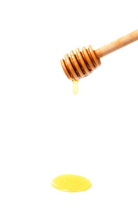 在白色背景下的蜂蜜勺子。蜂蜜从木勺流出。特写