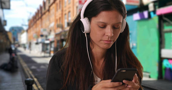 在城市街道上听音乐和打电话发短信的千禧一代妇女