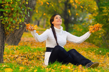女孩向干燥的秋天树叶扔在空气中
