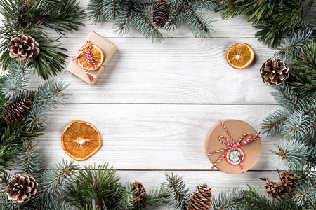 创意框架由圣诞树树枝在白色木背景与礼品盒, 松果。圣诞节和新年主题。平面布局, 顶部视图