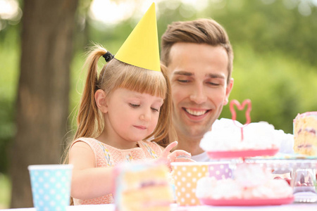 可爱的小女孩与父亲吃蛋糕在生日聚会户外