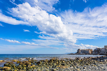 石头海滩在海湾与塔和村庄在其码头和暴风雨云在天空