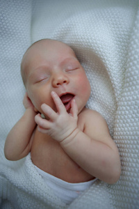 七天大的婴儿在后面睡觉。孩子被裹在毯子里, 在睡梦中表达情感。特写