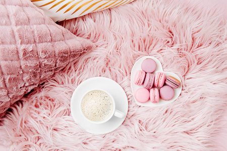 杯咖啡和马卡龙在盘子上粉红色蓬松羽绒被