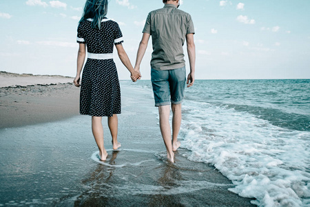 年轻的情侣走在沙滩附近的海边和牵手一起, 海滩暑假