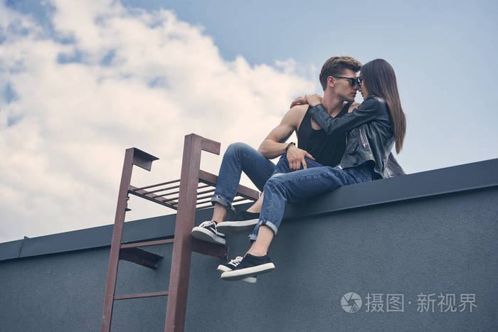 美丽的异族情侣的底部视图坐在屋顶上亲吻