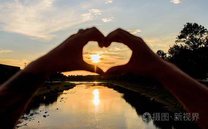 夕阳的阳光浪漫的气氛.男性手在心脏形状手势象征爱情和浪漫.