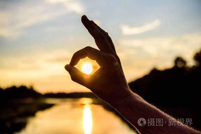 照片 剪影ok 手手势在日落前面在河水面之上.夕阳的阳光浪漫的气氛.