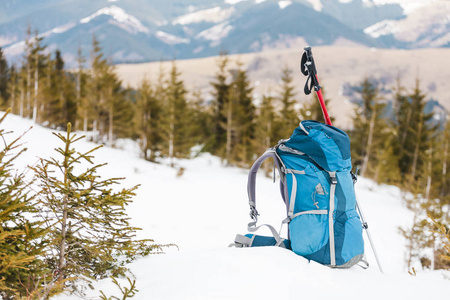背包在白雪覆盖的山脉和蓝天的背景下。在雪地上的背包。积极的生活方式。冬天徒步旅行。徒步旅行设备。徒步棍