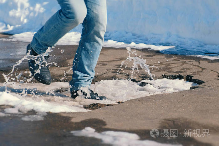 男人用脚踩在沥青上的雪水坑里.特写腿