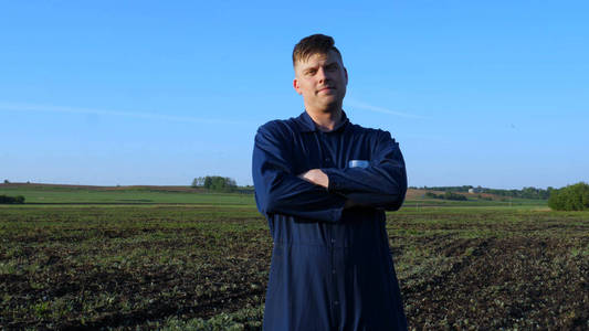 一个穿着蓝色长袍的年轻农夫走在田野里看着种植的植物。理念 清洁空气, 生物, 农业