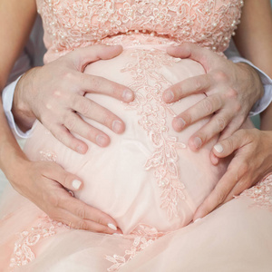 穿着粉色衣服的孕妇手放在肚子上。怀孕生育准备和期待的概念。特写, 室内。美丽的怀孕