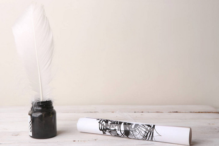 墨水瓶用羽毛和纸滚筒与墨画。白木桌上墨瓶上画书法和白羽毛的纸辊