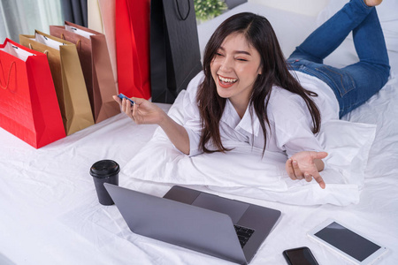 愉快的妇女使用笔记本电脑在线购物与信用卡在床上