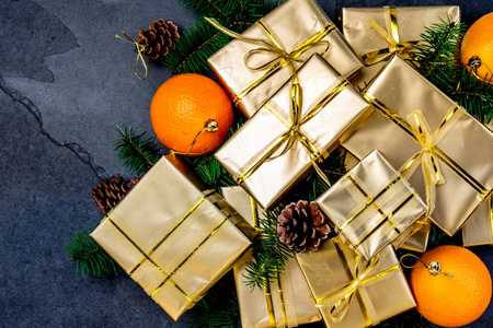 圣诞背景。金色礼品盒和圣诞装饰桔子, 圣诞树树枝和锥体在石板背景。平躺, 顶部视图