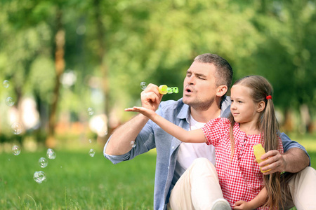 快乐的父亲和女儿吹肥皂气泡在公园里