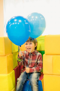 带着气球微笑的男孩。那男孩拿着球坐在游戏室里。孩子显示语言